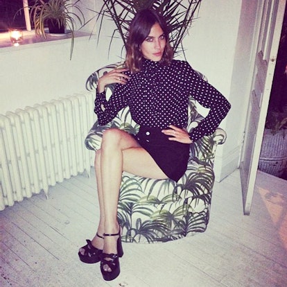 Alexa Chung posing in a black silk blouse, black skirt, and black candy sandals
