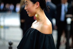 A woman standing in a black dress with a big golden circle shaped earring 
