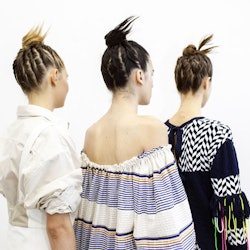 Three girls with braid buns posing with their backs turned