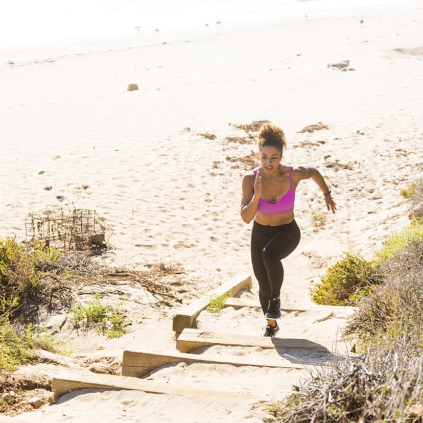 A woman running at a beach in a pink top and black leggings 