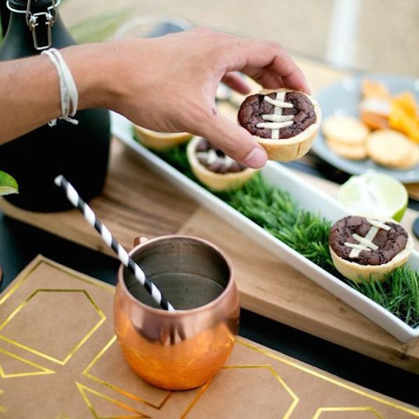 A person arranging muffins shaped like football on a tray for a party