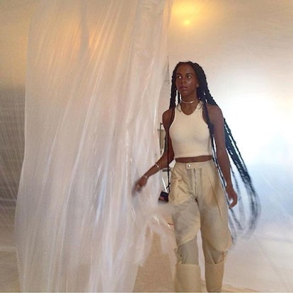 Juliana Huxtable in a white tank top and beige cargo pants posing next to the PVC curtain