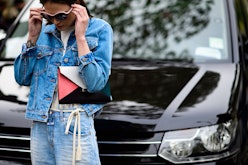 A woman standing in front of her car in a denim jacket, white tee and light blue jeans