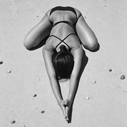 A woman stretching her body on a sand beach while wearing a bikini