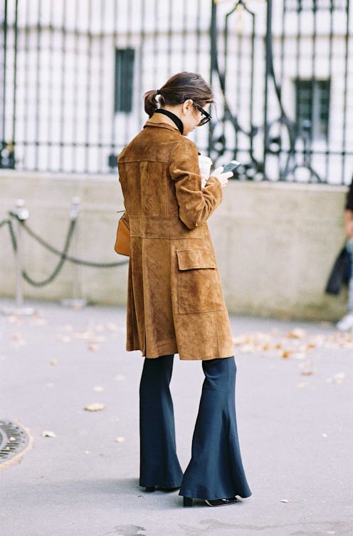 A back of a woman in a caramel suede coat and black flared pants