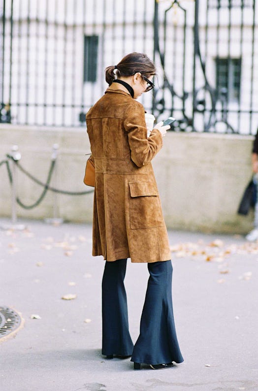 A back of a woman in a camel suede coat and black flared pants