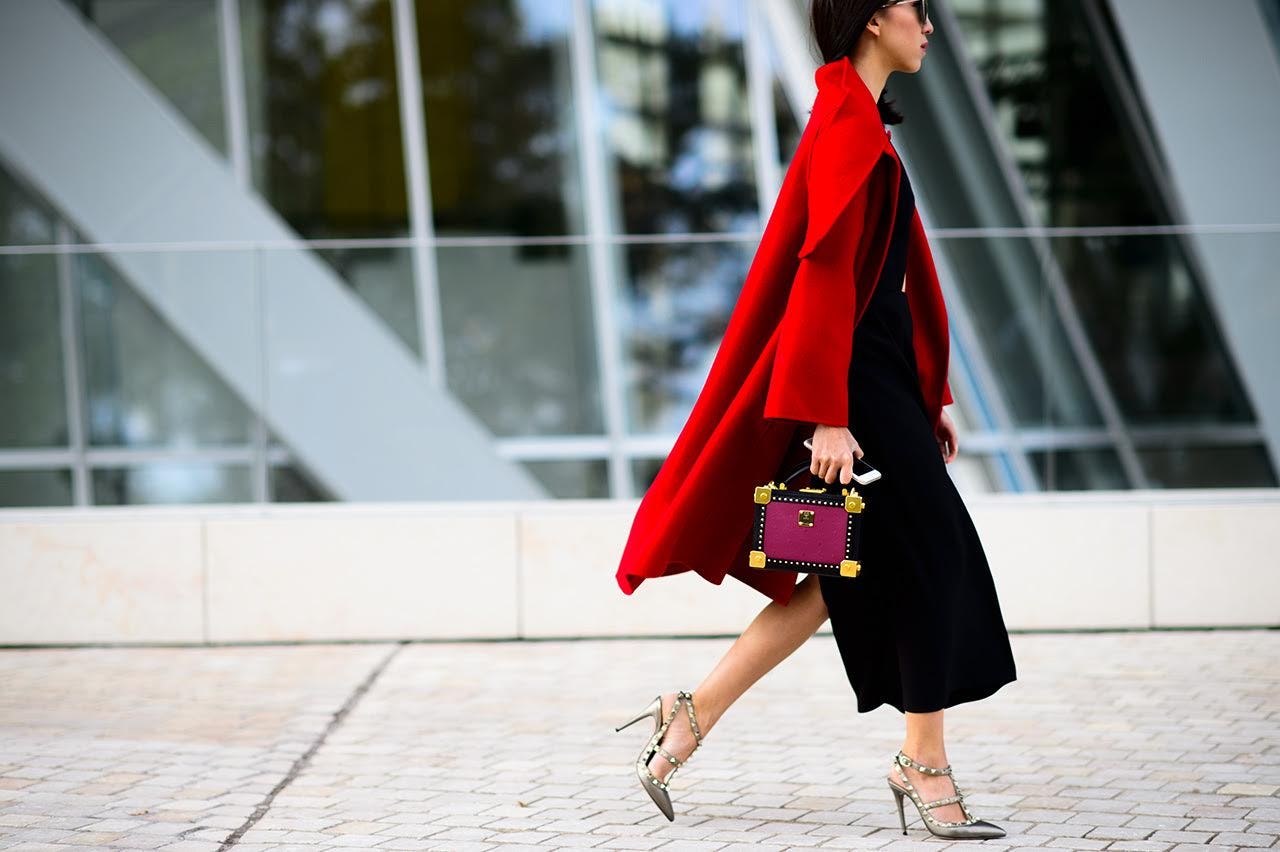 A woman wearing a black midi dress and a red coat for a winter wedding
