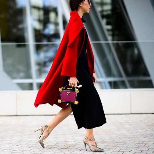 A woman wearing a black midi dress and a red coat for a winter wedding