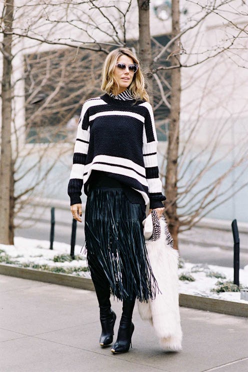 A woman in a sweater, black pants and a party dress under the sweater