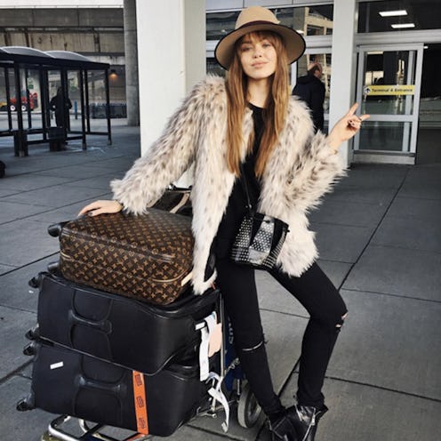 A woman posing at the airport leaning against a trolley with three suitcases on it 
