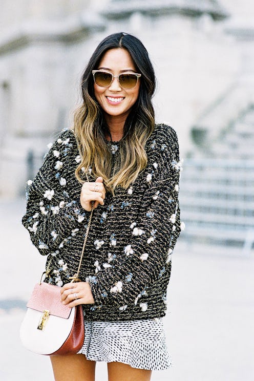 A woman wearing an oversize sweater in black and white, a floral mini skirt, and a pink purse