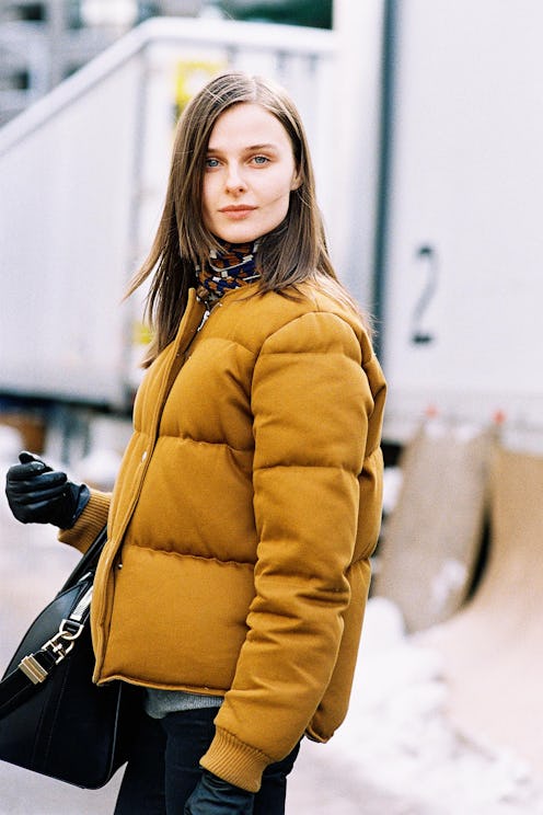 A model in a yellow puffy coat, with black leather gloves and a black bag 