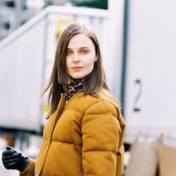 A model in a yellow puffy coat, with black leather gloves and a black bag 