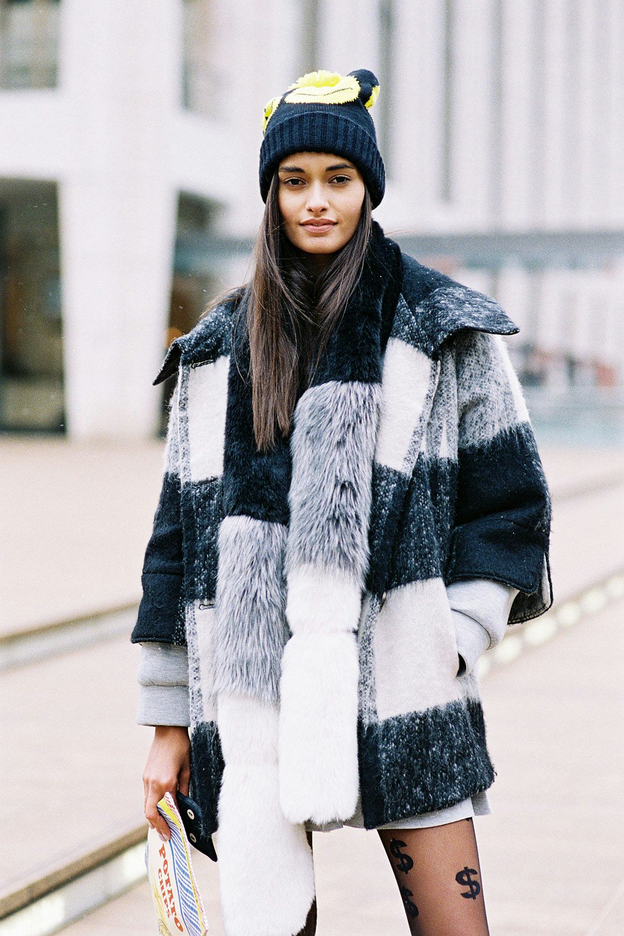Young black-haired lady posing in a white, grey, and black fur coat and in a black cap