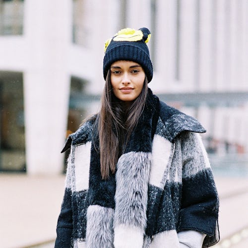 Young black-haired lady posing in a white, grey, and black fur coat and in a black cap