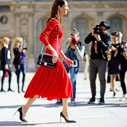 A woman walking on the street in a red Valentine's Day dress, a black bag and black heels 