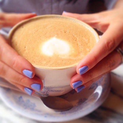 A woman holding a cup of latte with a periwinkle Coachella-ready manicure done