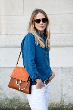 A woman in a denim button-up, white jeans, sunglasses and a brown bag
