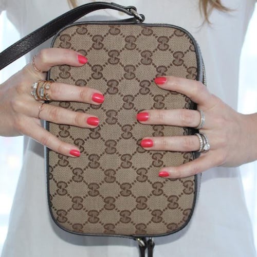 A closeup of hands with red nails holding a Gucci bag