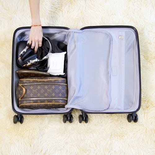 A person packing a carry-on suitcase, carefully organizing their makeup bags
