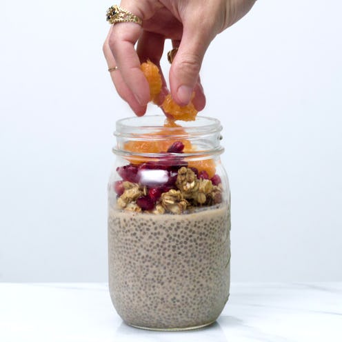 A hand putting diced orange in Chia seed pudding