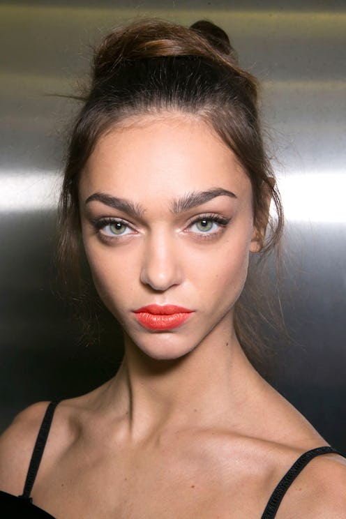 A model with her hair in a high bun wearing a coral lipstick