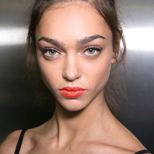 A model with her hair in a high bun wearing a coral lipstick