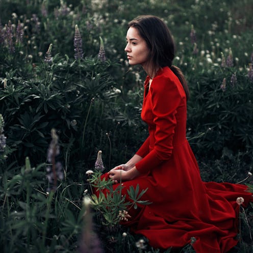 A woman sitting on the ground in a forest, wearing a red dress