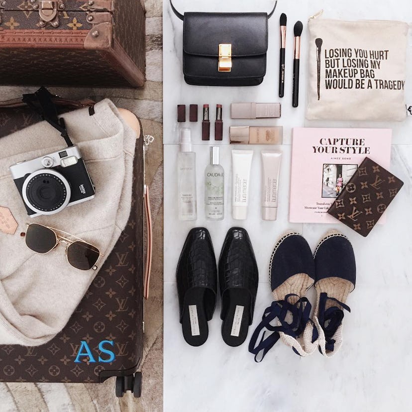 Two bags, two pairs of shoes, sunglasses, a camera, a wallet, and beauty makeup products stacked nex...