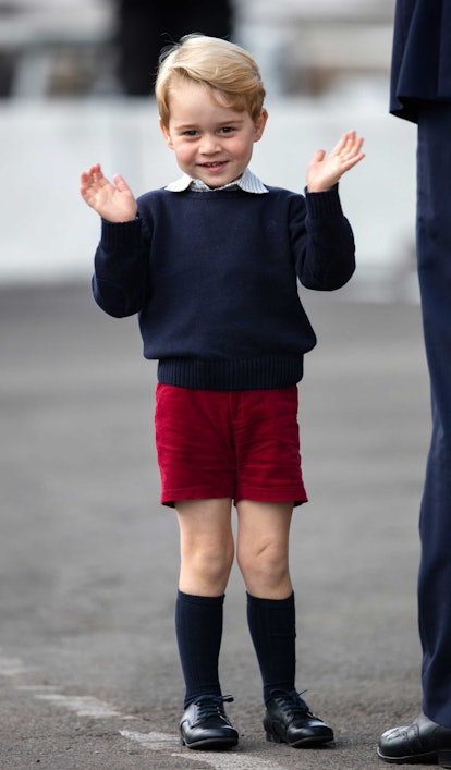Prince George wearing red shorts, a sweater over a shirt, knee-high socks and shoes.