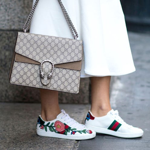 A closeup of a woman's feet in Gucci sneakers with a rose on the side and a Gucci bag