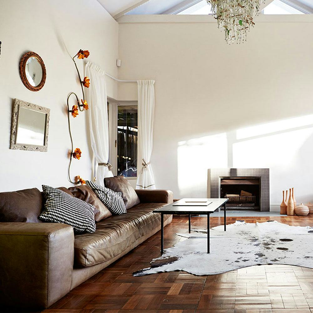 A living room with a brown leather furniture, black coffee table, small fireplace, and an animal pri...