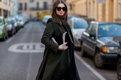 A woman in a long black coat standing in the middle of the street holding her black handbag