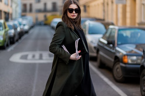A woman in a long black coat standing in the middle of the street holding her black handbag