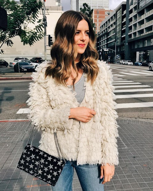 A woman with brown wavy hair standing outside in a puffy jacket and a purse with a star pattern