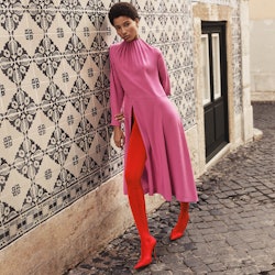 A model in a long pink dress, red leggings and red heels