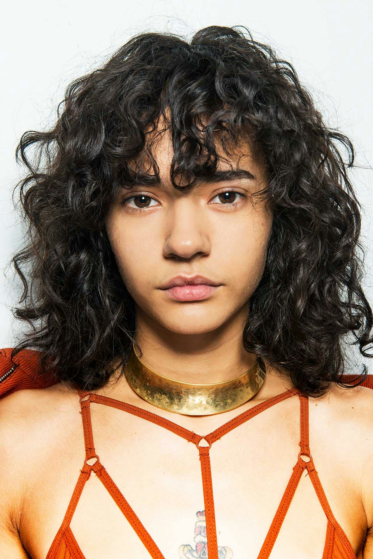 A curly-haired brunette woman who uses a shine-boosting shampoo