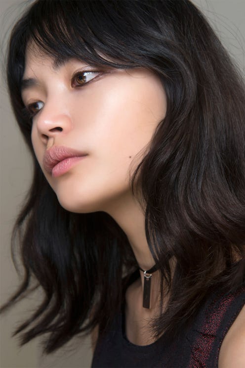 A model with black hair, a black sheer top and a black necklace poses while looking off into the dis...
