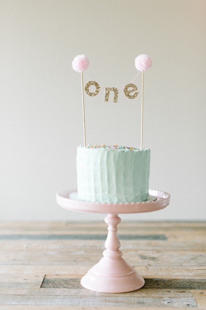 A birthday cake in mint green with paper decorations reading: 'One.'