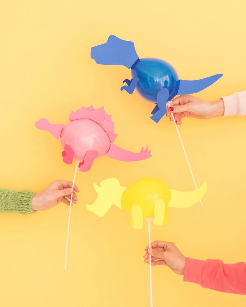 Kids holding dinosaur-shaped balloons in pink, yellow and blue on the sticks 