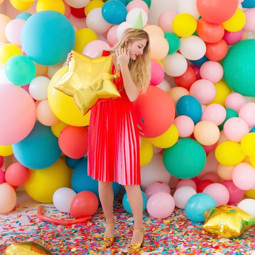 A girl in an orange dress, wearing a party hat while holding a star-shaped balloon standing in front...