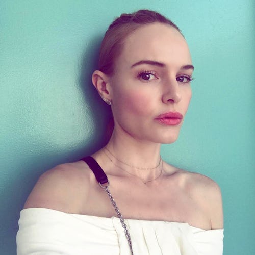 Kate Bosworth posing against a teal wall, wearing pink lipstick, and a white top
