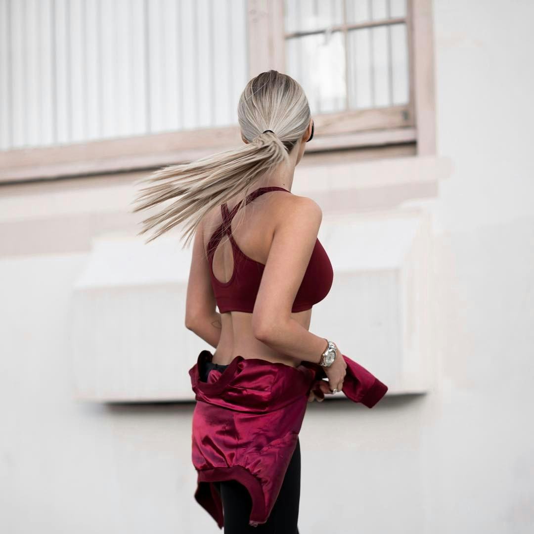 A woman standing in a red sports top and having a tracksuit tied around her waist