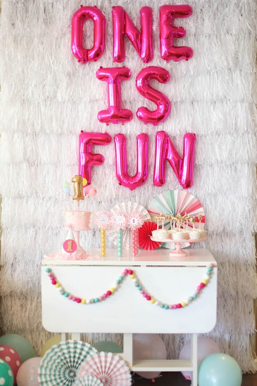 A decorated party area behind the food table with balloons in pink reading: 'One is fun.'