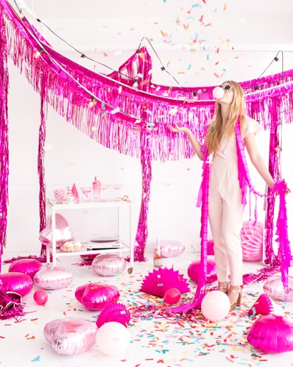A girl standing in a party-decorated room with an overhead display in pink and balloons and confetti...