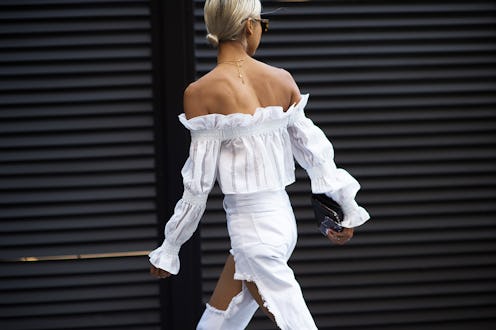 A blonde woman in a white frill top and white trousers walking 