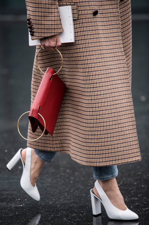 A woman in a brown check coat, white sling-back heels and a red statement bag