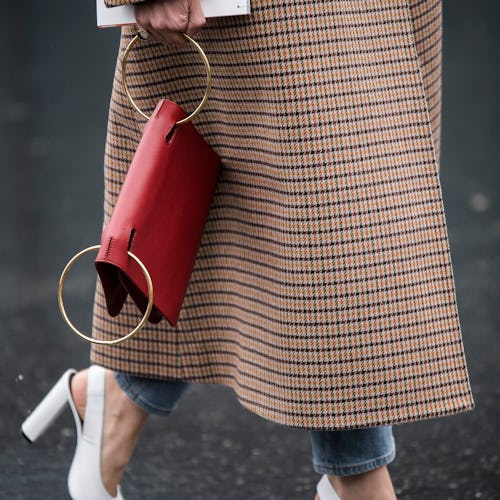 A woman in a brown check coat, white sling-back heels and a red statement bag 