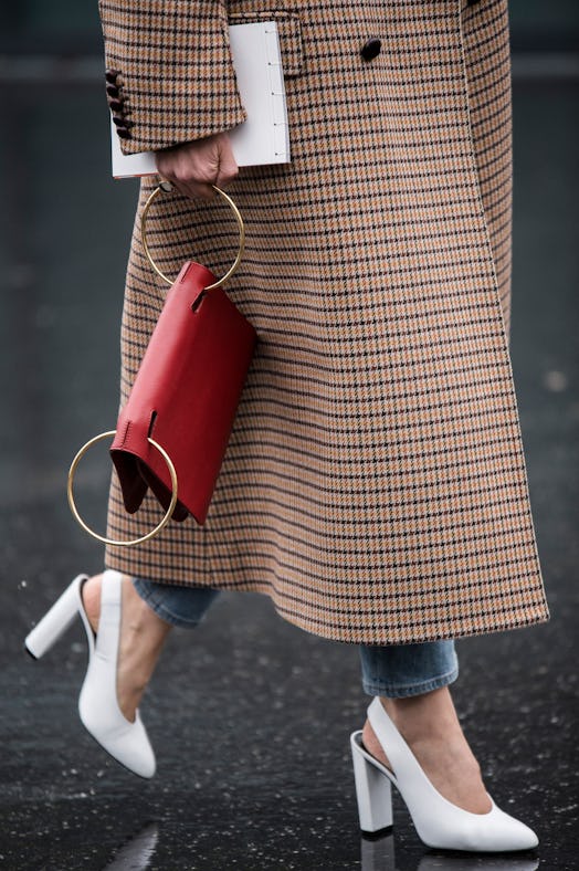 A woman in a brown check coat, white sling-back heels and a red statement bag 