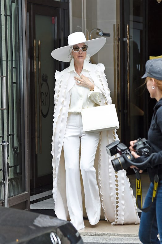 Celine Dion walking while wearing a white hat, shirt, coat, and pants